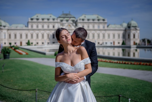 Free photo groom is kissing bride's neck in front of huge king  residential palace