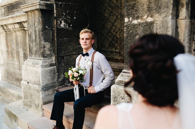 Free photo groom sitting on the stone steps and poses for the camera