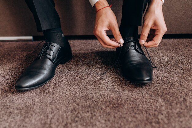 Groom ties laces on his shoes sitting on a sofa