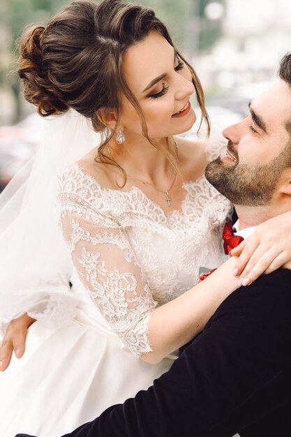 Groom on wheelchair holds bride on his knees sitting outside in the park