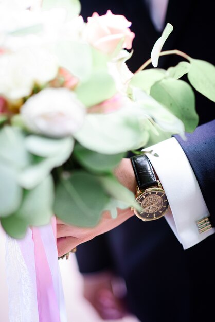 Groom with golden watch holds green wedding bouquet 