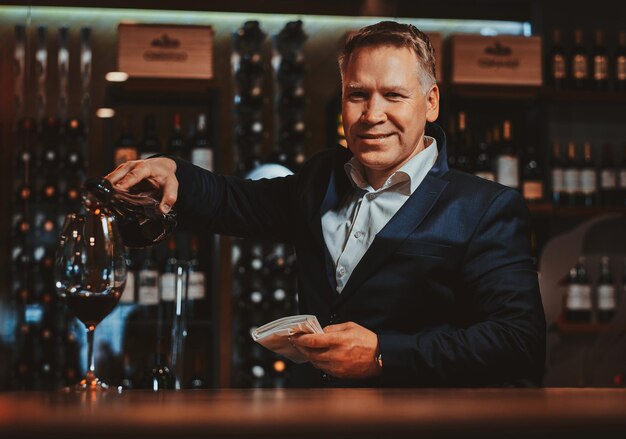 Groomed elegant wine sommelier is pooring red wine to the glass to taste it.