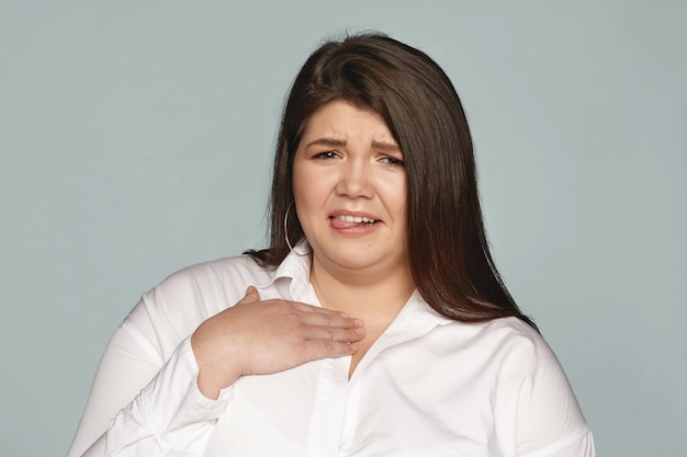 Gross, Ew. Portrait of emotional displeased young chubby European woman grimacing, sticking out tongue and holding hand on her chest, feeling sick because of disgusting smell. Bad odor and disgust