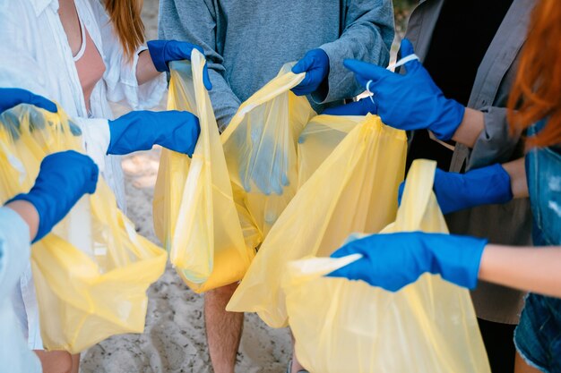 Group of activists friends collecting plastic waste on the beach. Environmental conservation.