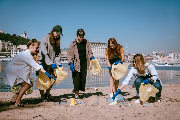 Group of activists friends collecting plastic waste on the beach. Environmental conservation.
