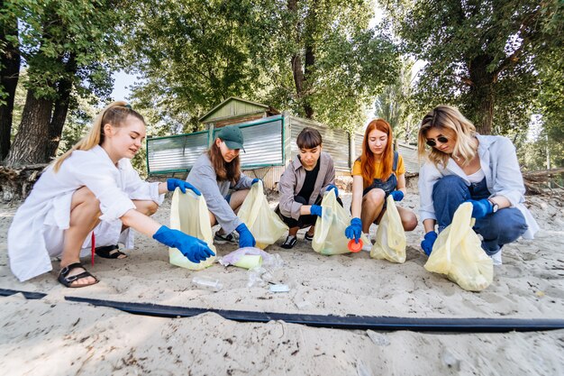 Group of activists friends collecting plastic waste on the beach. Environmental conservation.