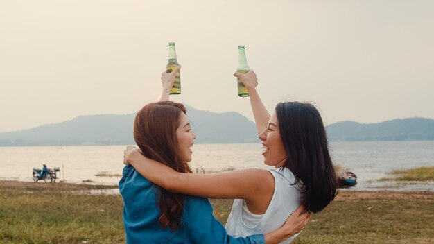 술을 마시는 아시아 소녀 커플의 가장 친한 친구 십대들은 캠프장에서 함께 즐거운 시간을 보내며 병 맥주의 경례 건배를 즐깁니다.
