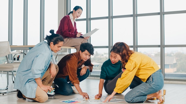 Gruppo di giovani creativi asiatici in abbigliamento casual discutendo di idee riunione di brainstorming di affari piano di progetto di progettazione di software applicativo mobile disposto sul pavimento in ufficio. concetto di lavoro di squadra del collega.