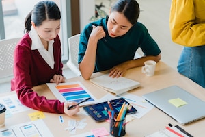 Group of asia young creative people japanese female boss supervisor teaching intern or new employee hispanic girl helping with difficult assignment in modern office. coworker teamwork concept.