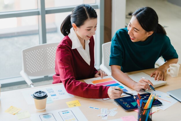 Group of Asia young creative people Japanese female boss supervisor teaching intern or new employee hispanic girl helping with difficult assignment in modern office. Coworker teamwork concept.