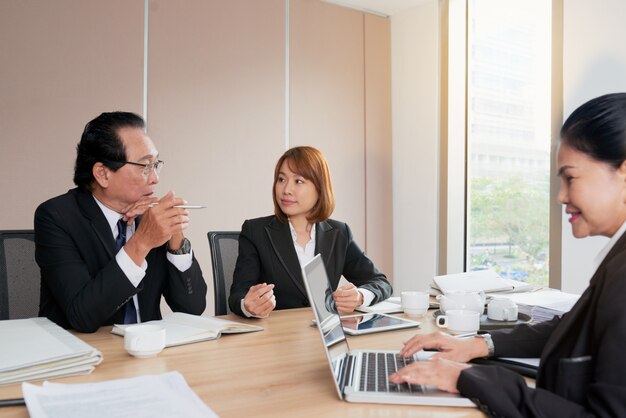 Group of Asian business people sitting around meeting table and talking