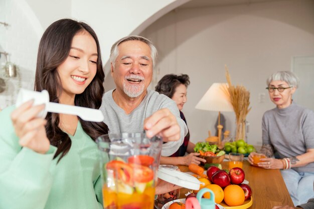 집에서 저녁 식사 파티에서 아시아 노인 노인 그룹 노인 친구는 딸과 함께 샐러드와 과일 주스를 준비하고 노인 친구와 웃으면서 즐거운 순간 대화를 나누며 웃고 있습니다.