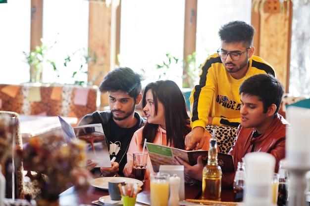 Free photo group of asian friends sitting cafe happy indian people having fun together sitting on couch and choose meals from the menu