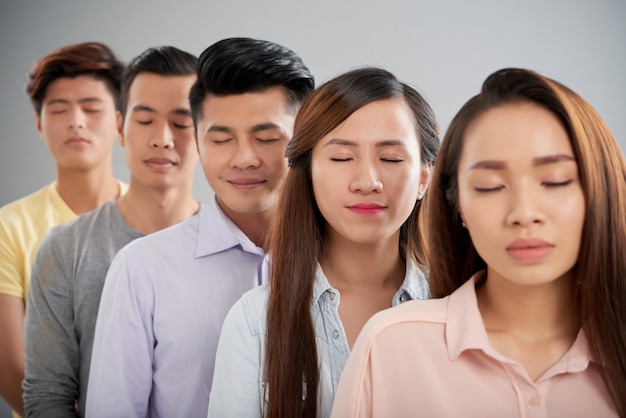 Группа азиатских мужчин и женщин, стоящих в ряду с закрытыми глазами