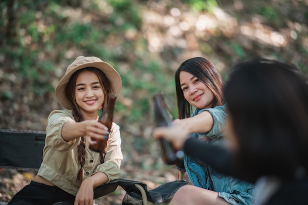 Group beautiful Asian women friends travelers relaxing at front of camping tent They enjoy to talking and drinking beer with fun and happy together