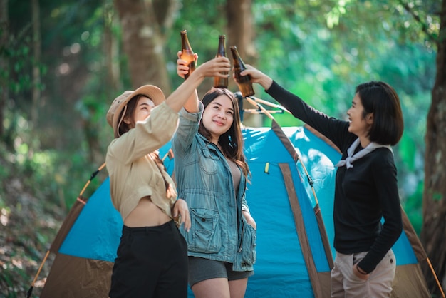 캠핑 텐트 앞에서 휴식을 취하는 아름다운 아시아 여성 친구 여행자들은 함께 즐겁고 행복하게 맥주를 마시며 이야기를 나누는 것을 즐깁니다.