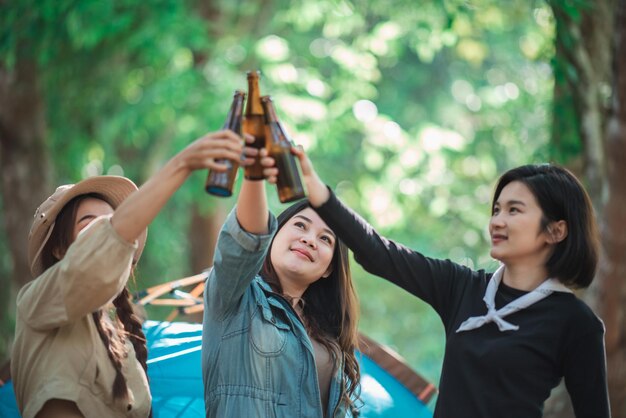 Group beautiful Asian women friends travelers relaxing at front of camping tent They enjoy to talking and drinking beer with fun and happy together