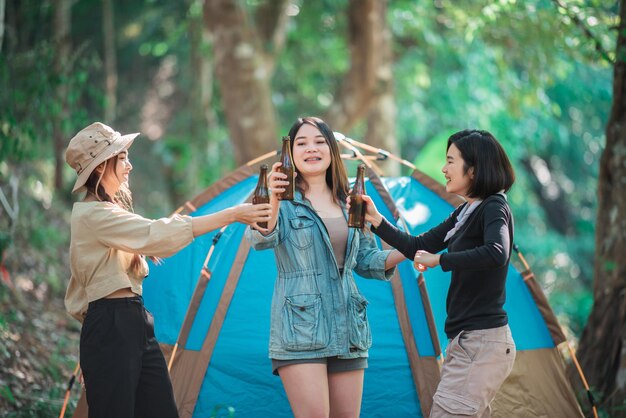 キャンプテントの前でリラックスする美しいアジアの女性の友人の旅行者をグループ化する彼らは一緒に楽しく幸せにビールを話したり飲んだりするのを楽しんでいます