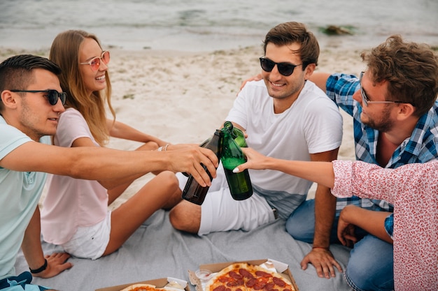 Group of best friends making a toast, drinking beer while having fun on the beach