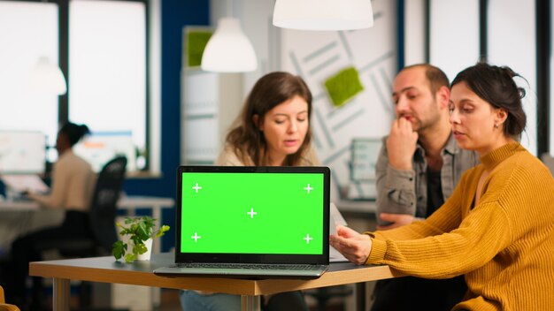 Group of business people discussing company plan with mockup laptop in front of camera, pc ready for financial project presentation placed on desk. Leader using green screen pc with chroma key display