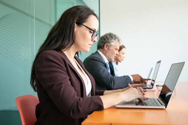 Group of business people sitting in line and using computers in office. Employees of different ages typing on laptop keyboards.