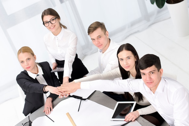 Group of business people stacking each other's hand over the desk