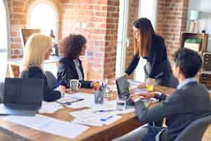 Free photo group of business workers smiling happy and confident working together with smile on face young beautiful woman standing explaining documents at the office