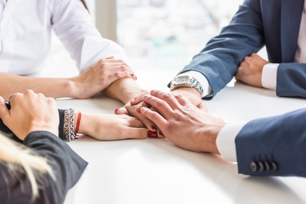 Group of businesspeople stacking each other's hand on white desk