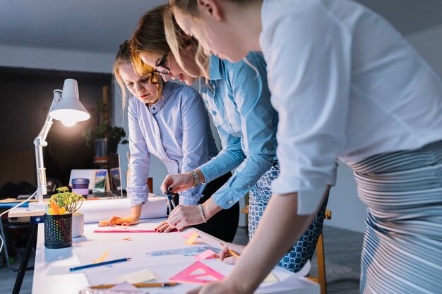 Group of businesswomen drawing plan on white paper with instruments over desk at workplace