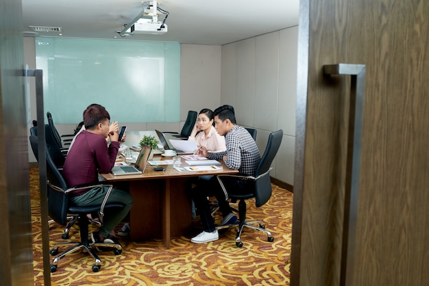 Group of casually dressed colleagues sitting in office behind open door and talking
