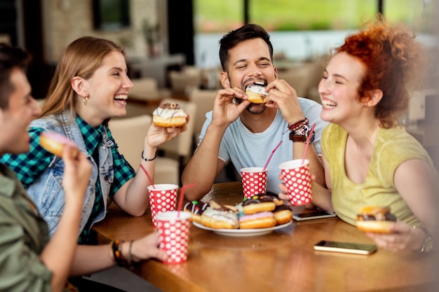 Free photo group of cheerful friends eating donuts in a cafe