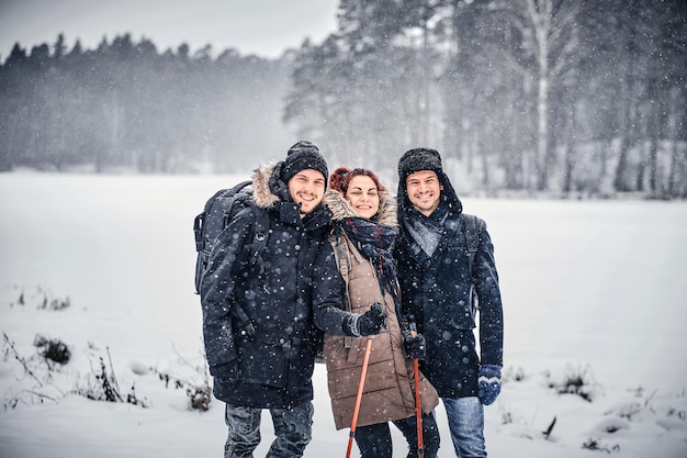 함께 즐거운 시간을 보내는 쾌활한 친구 그룹, 서로 옆에 서서 카메라를 바라보고 눈 덮인 숲에서 하이킹