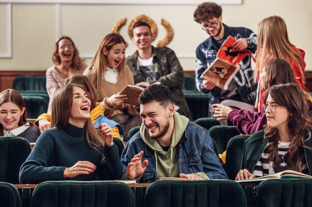 レッスン前に講堂に座っている陽気な幸せな学生のグループ