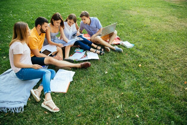 Группа веселых студентов подростков в случайных нарядах с записными книжками и ноутбуком
