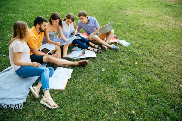 Group of cheerful students teenagers in casual outfits with note books and laptop
