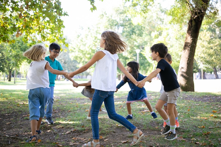 Free Photo group of children holding hands and dancing around, enjoying outdoor activities and having fun in park. kids party or friendship concept