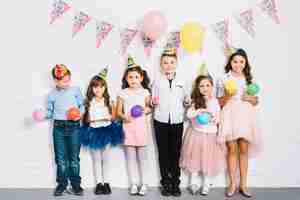 Free photo group of children standing against wall holding balloons in hand at birthday party