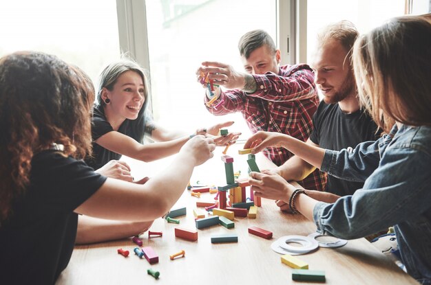 木製のテーブルに座っている創造的な友人のグループ。人々はボードゲームをしている間楽しんでいました。
