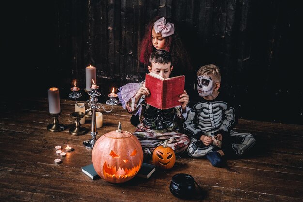 ハロウィーンパーティー中に、古い家でホラーストーリーを読んで怖い衣装を着たかわいい多民族の子供たちのグループ。ハロウィーンのコンセプト。