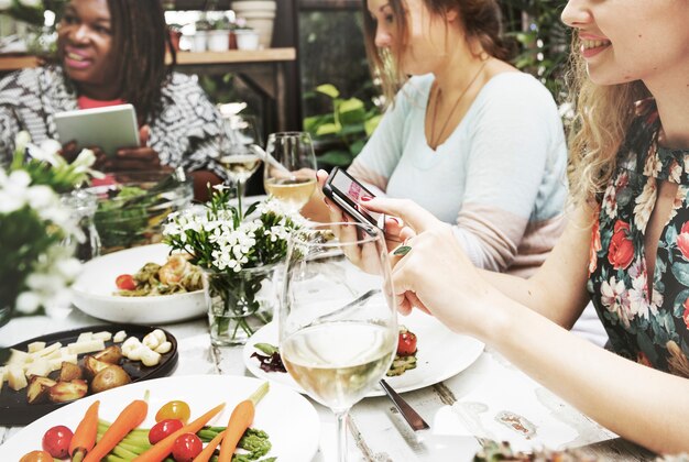 Группа разнообразных женщин, имеющих еду вместе с использованием цифровых устройств