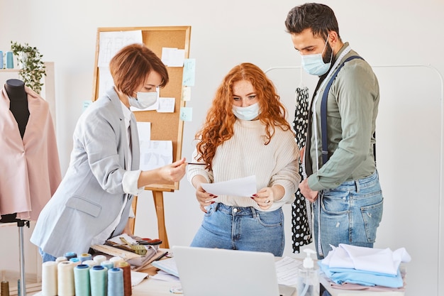 Gruppo di stilisti che lavorano in atelier con maschere mediche e carta