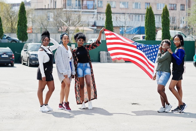 Un gruppo di cinque donne afroamericane che camminano insieme sul parcheggio con la bandiera degli stati uniti