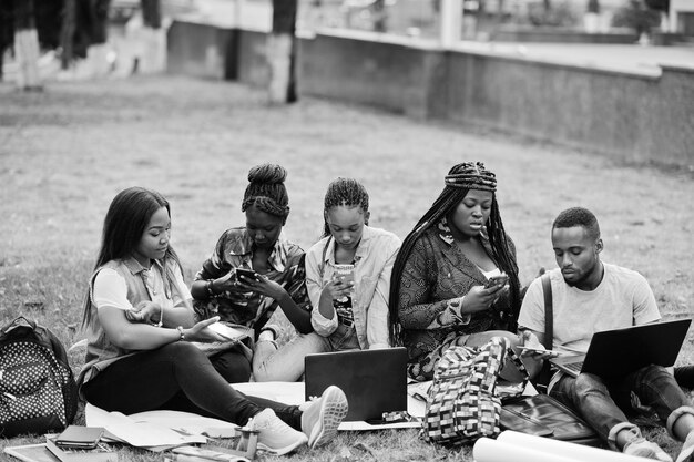 大学の校庭でキャンパスで一緒に時間を過ごす5人のアフリカの大学生のグループ携帯電話で作る黒人のアフロの友人教育のテーマ