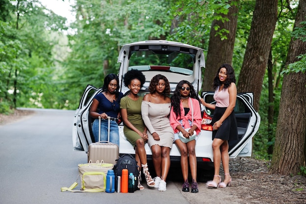 Free photo group of five happy african american traveler girls sitting in car open trunk