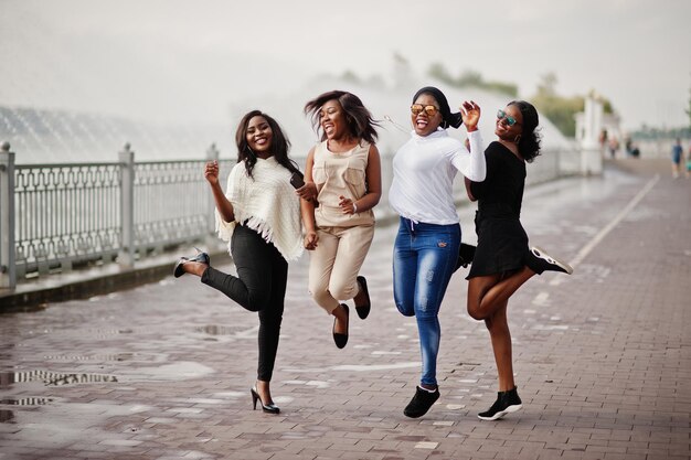 Group of four african american girls having fun and jumping against lake with fountains