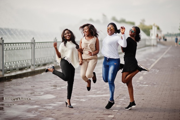Группа из четырех афроамериканских девушек веселятся и прыгают у озера с фонтанами
