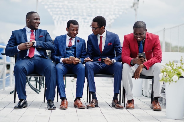 Free photo group of four african american happy succesfull mans at suit rich black business mans sitting at chairs looking at mobile phones