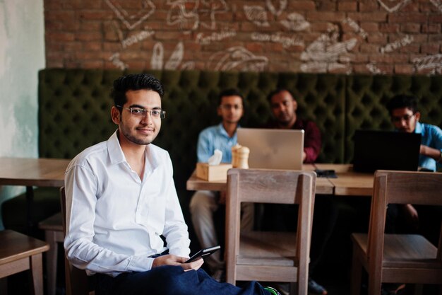 Group of four south asian men's posed at business meeting in cafe Indians work with laptops together using various gadgets having conversation Indian man with mobile phone