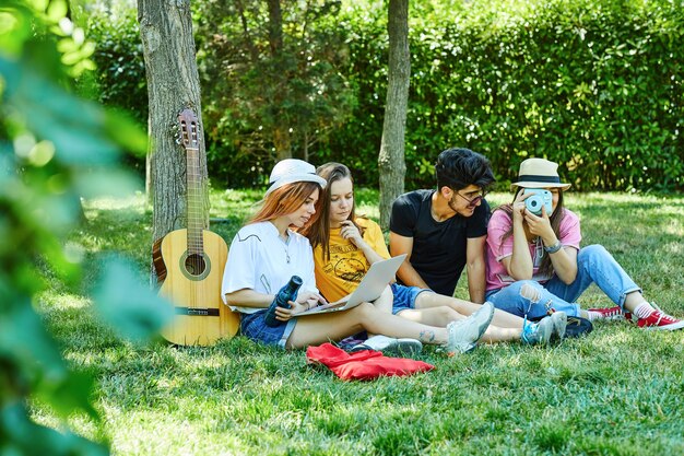 Group of four young people having fun in park, sitting on the grass