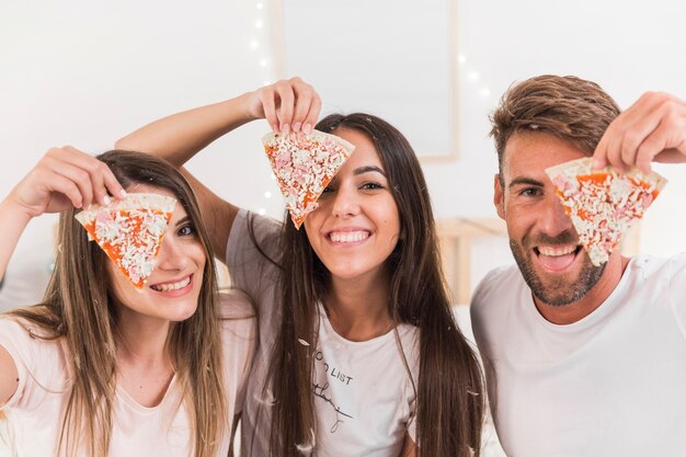 Группа друзей, покрывающих их один глаз кусочком пиццы